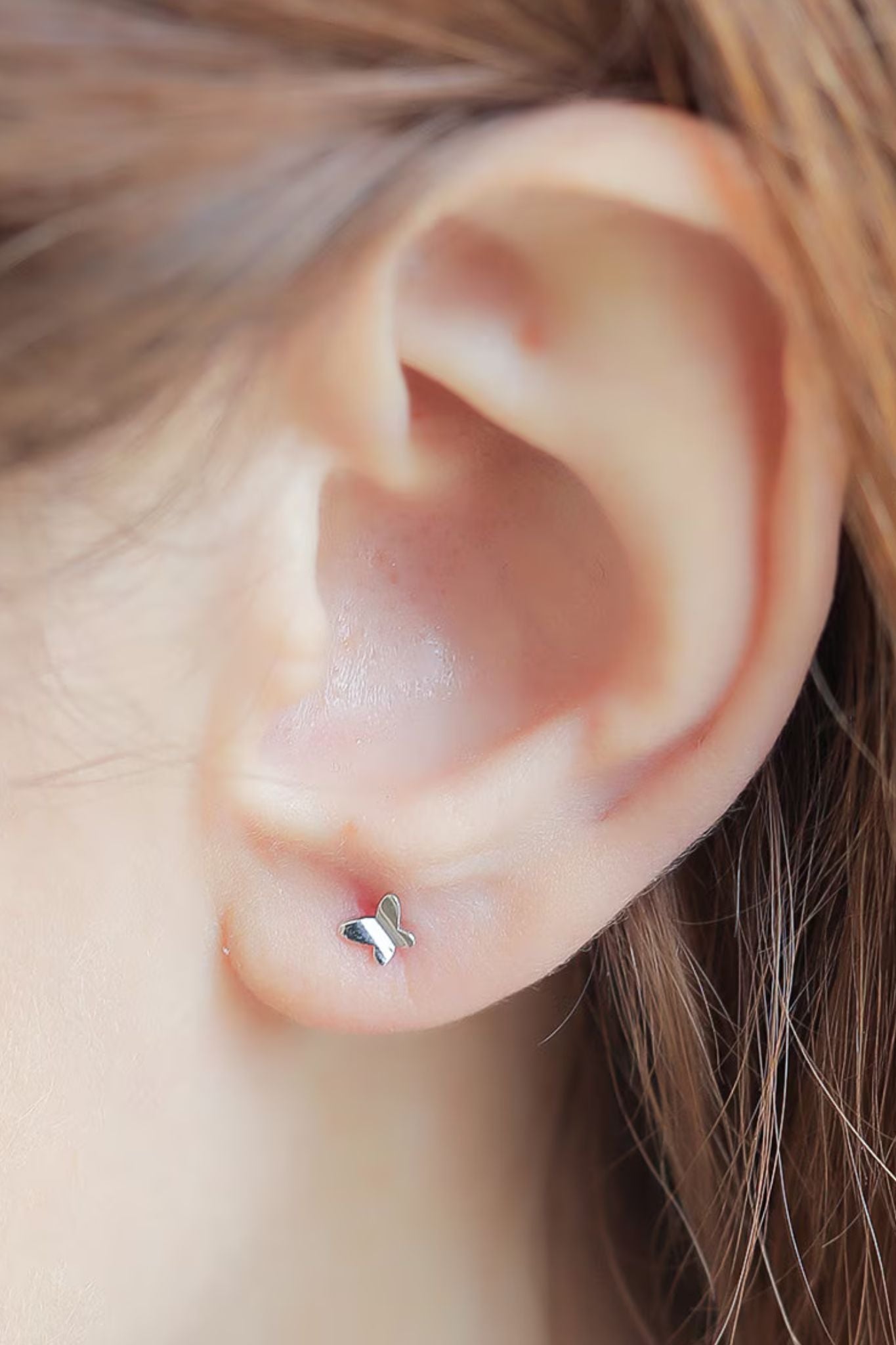 model wearing a silver tiny butterfly stud earring in the earlobe, showing the dainty size of the earrings